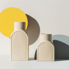 two white vases sitting next to each other in front of a yellow and grey circle