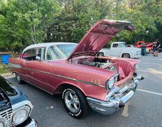 an old car with its hood open parked in a parking lot next to other cars