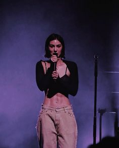 a woman standing on top of a stage holding a microphone in her hand and wearing high waist jeans