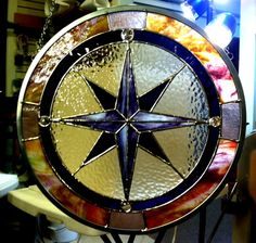 a stained glass compass is displayed on a stand in front of a wall with other items