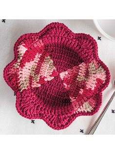 a crocheted dishcloth with pink and white flowers on it next to a spoon