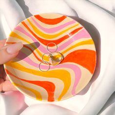 two wedding rings are placed on top of an orange and pink striped ring dish that is being held by someone's hand