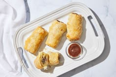 three pastries on a tray with dipping sauces and a fork next to them