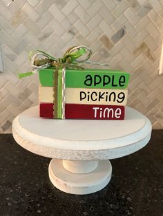 a stack of books sitting on top of a white cake stand with a green bow