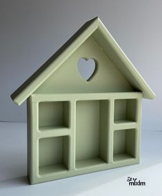 a small green house with a heart cut out of it's window and shelves