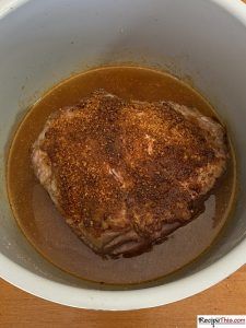 a piece of meat in a bowl with brown sauce on the side and seasoning