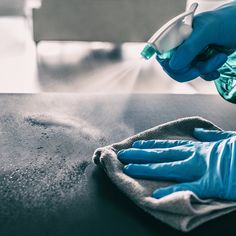 a person in blue gloves is cleaning a table with a microfiber and cloth