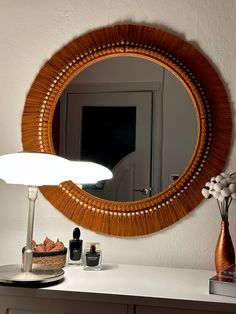 a round mirror sitting on top of a white dresser next to a lamp and vase