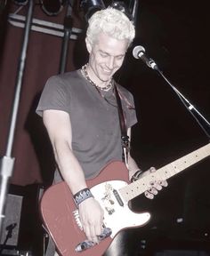 a man with white hair playing an electric guitar in front of a microphone on stage