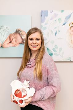 a woman holding a baby in her hands while standing next to two paintings on the wall