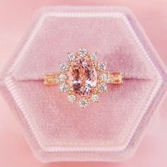 a pink diamond ring sitting on top of a velvet display case with white and yellow diamonds