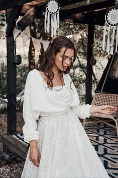 a woman in a white dress is standing near a table and some hanging tassels