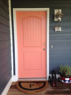 a pink door on the side of a house with two planters next to it