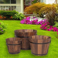 four wooden buckets sitting on top of green grass in front of flowers and bushes