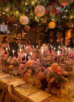 a group of people sitting around a table with candles in the middle and flowers on it