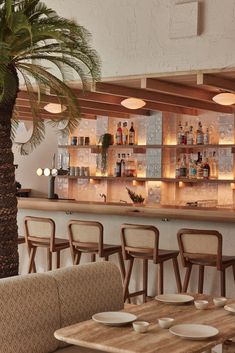 an empty restaurant with wooden tables and chairs next to a palm tree in front of the bar