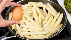 a person holding an egg in a frying pan on the stove with other food