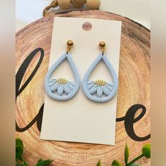 a pair of blue earrings with white flowers on them sitting on top of a piece of wood