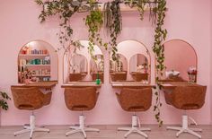 the salon is decorated with pink walls and greenery hanging from the ceiling, along with three round mirrors