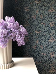 a vase with purple flowers sitting on a table next to a wallpapered wall