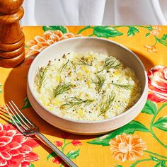 a white bowl filled with food next to a fork and knife on a yellow floral table cloth