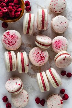 raspberry macaroons with white and red frosting next to a bowl of raspberries