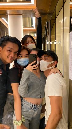 four people wearing masks taking a selfie in front of a mirror with their cell phone