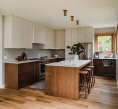 a kitchen with wooden flooring and white cabinets, counter tops and stools next to an island