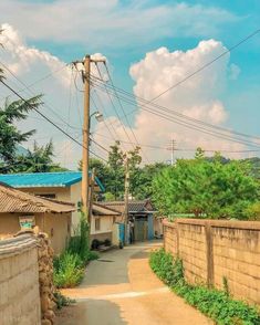 an alley way with power lines above it and houses on the other side, in front of a cloudy blue sky