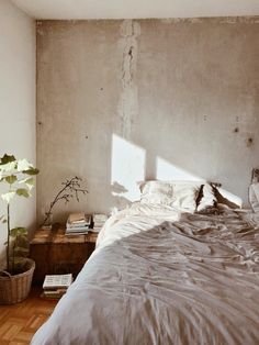 an unmade bed sitting in a bedroom next to a wooden table and potted plant