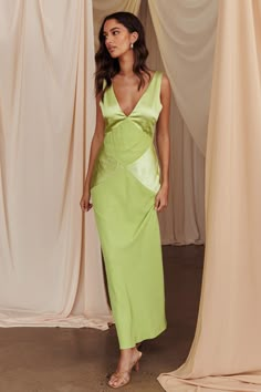 a woman standing in front of curtains wearing a lime green dress and matching heels with her hand on her hip