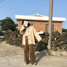 a woman standing in front of a brick building while holding up a book to her face