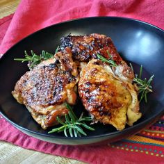 two pieces of meat sitting in a black bowl on a red towel next to a wooden table