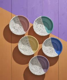 four different colored bowls sitting on top of a wooden table next to a purple and orange wall