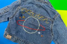 upcycled kids denim jackets w/ custom hand embroidered lettering! ✍🏼 this item combines my passions for sustainable fashion, eye-catching embroidery design, and all things denim! 👖the back of each of these denim jackets is hand stitched with child's name above a space design!🧵 🪐 i source high quality preloved denim from various brands. item will be long sleeve, medium to heavy weight blue denim. exact branding, color, wash, and details of jacket will vary based on what i have on hand in your Hand Embroidered Denim, Baby Denim Jacket, Kids Jeans Jacket, Kids Denim Jacket, Personalized Jacket, Embroidered Jean Jacket, Denim Embroidery, Planet Design, Kids Jackets