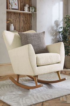 a white rocking chair sitting on top of a wooden floor next to a potted plant