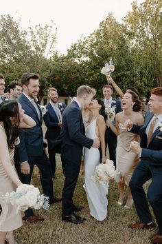 a group of people standing around each other in front of some trees and one person holding a bouquet