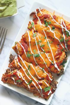 two slices of lasagna on a white plate with sauce and green guacamole