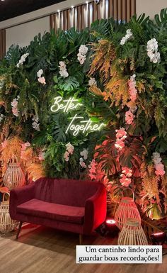 a red couch sitting in front of a green wall with flowers and plants on it