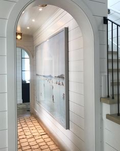 an arched doorway leads to a hallway with white walls and wood flooring, along with a painting on the wall