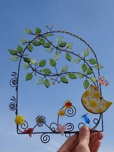 a hand holding up a metal sculpture with flowers and birds on it