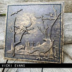 a metal plaque with an image of birds and bats on it, sitting on a wooden surface