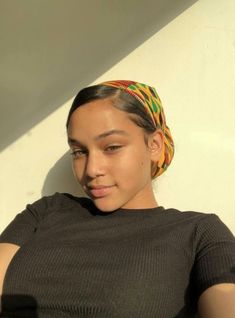 a woman with a colorful head wrap on her head sitting in front of a white wall