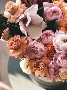 a white vase filled with lots of pink and orange flowers on top of a table