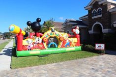 an inflatable mickey mouse bouncer is on the grass near a driveway and house