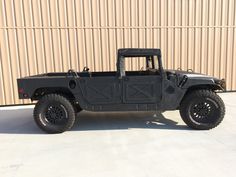 a black jeep is parked in front of a building with a tan wall behind it