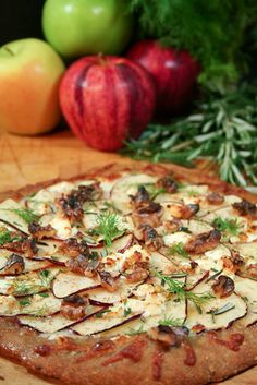 a pizza sitting on top of a wooden cutting board next to apples and pine cones