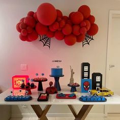 a table topped with red balloons and spiderman cake toppers next to other decorations