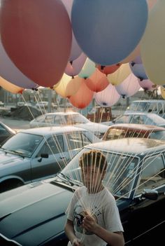 a person holding up balloons in front of parked cars