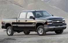 a black pickup truck parked in the middle of a dirt field with mountains in the background